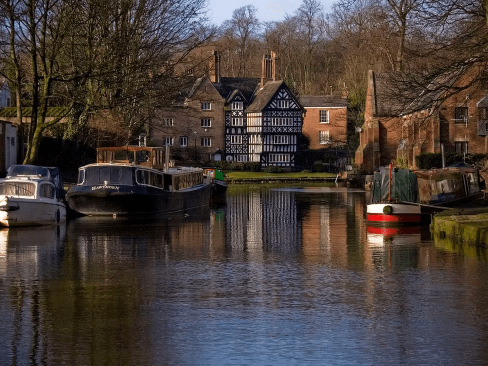 Canal with moored boats and a historic half-timbered building in the background.