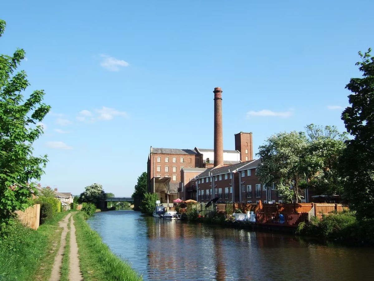 Canal with path, brick buildings, and chimney under a blue sky.