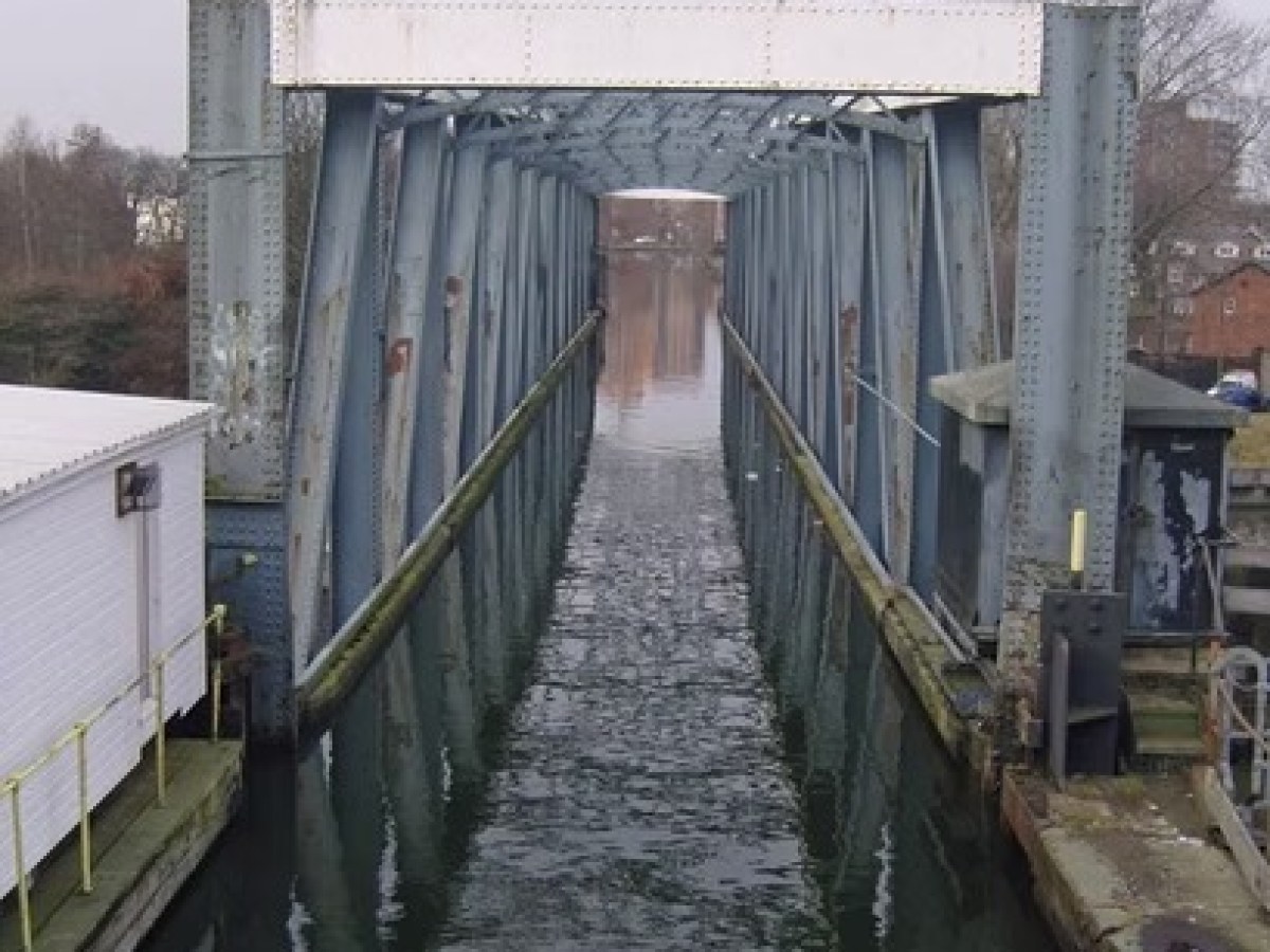 Narrow canal passing through a steel bridge with overcast sky.