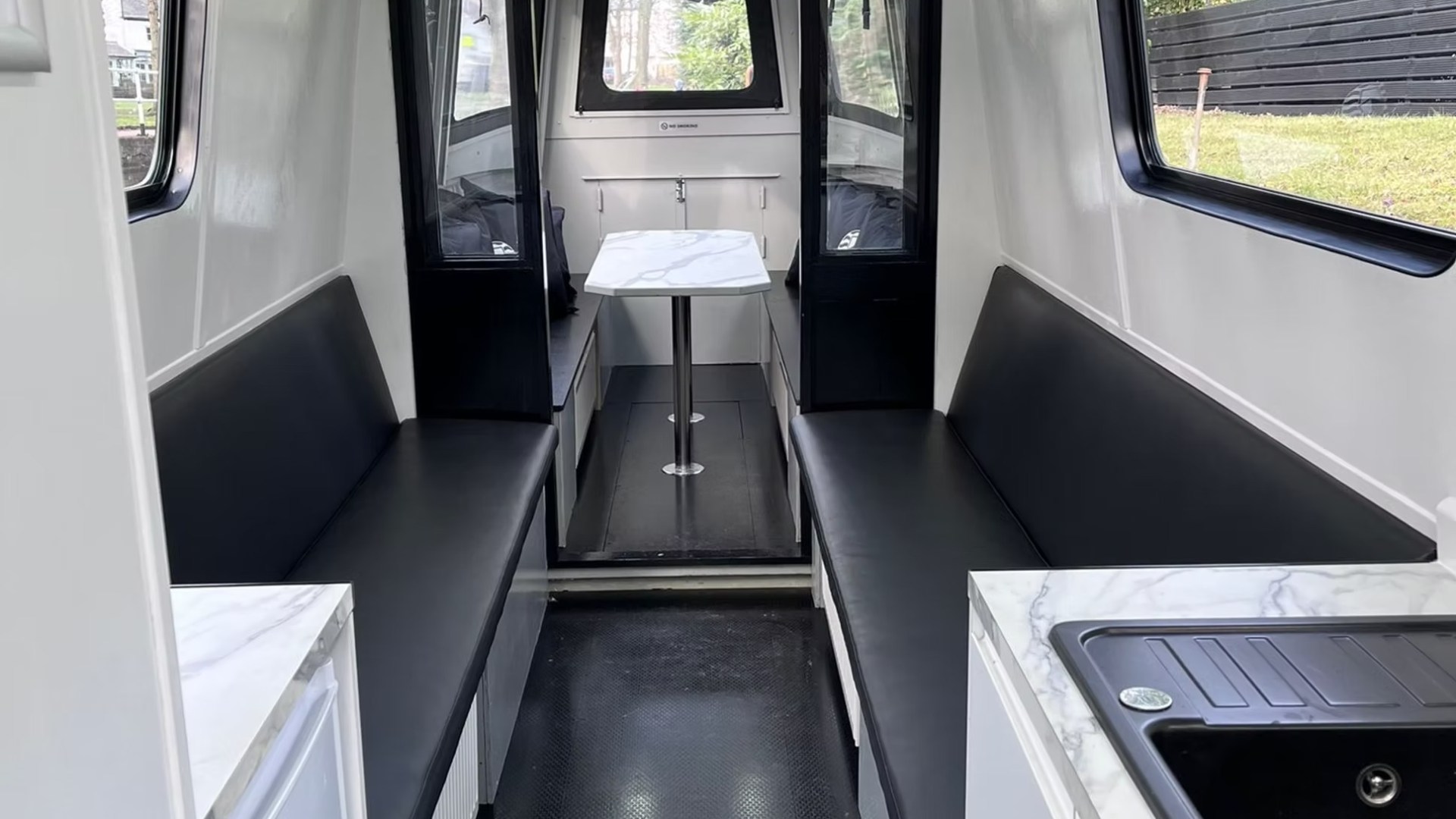 Interior of a white vehicle with black benches, a table, and emergency exit sign.