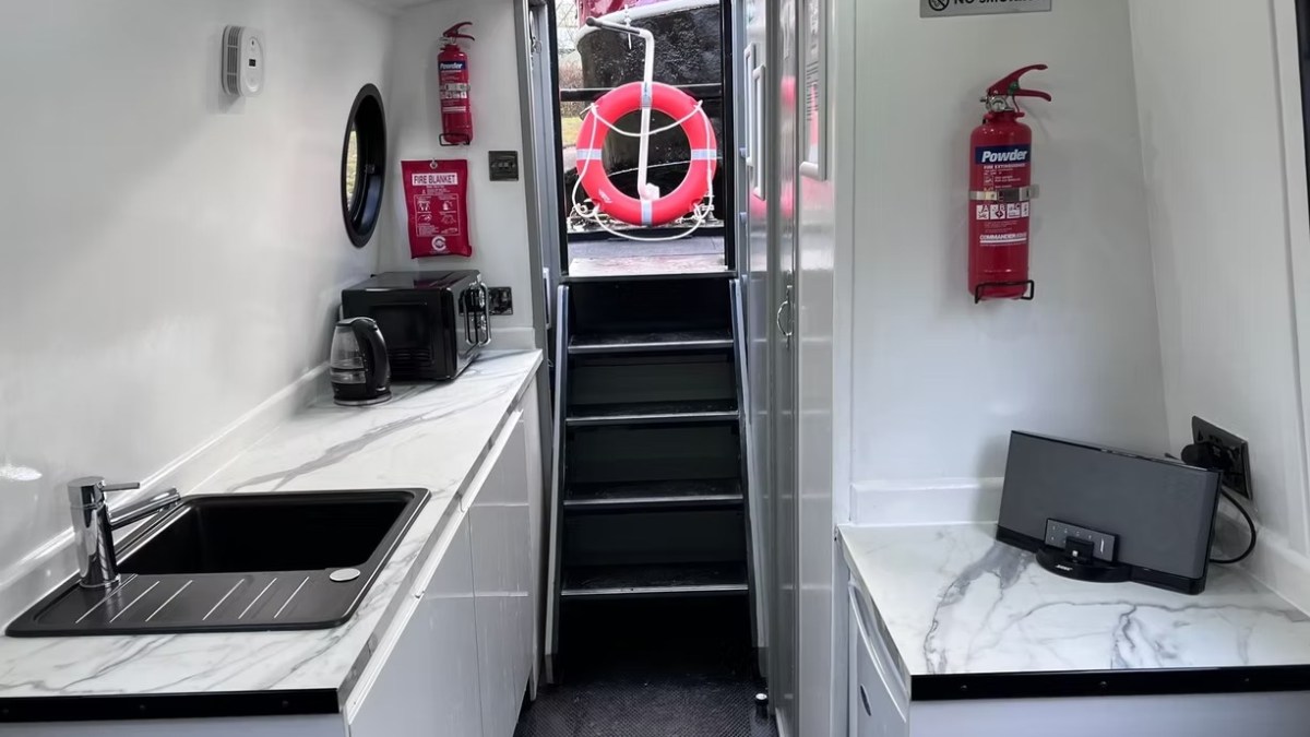 Boat interior with kitchenette, fire extinguishers, and stairs leading outside.