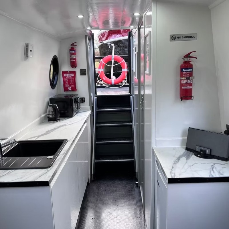 Boat interior with kitchenette, fire extinguishers, and stairs leading outside.