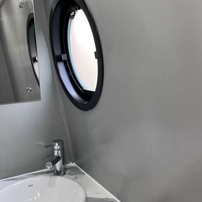 Bathroom sink with porthole window and mirror.