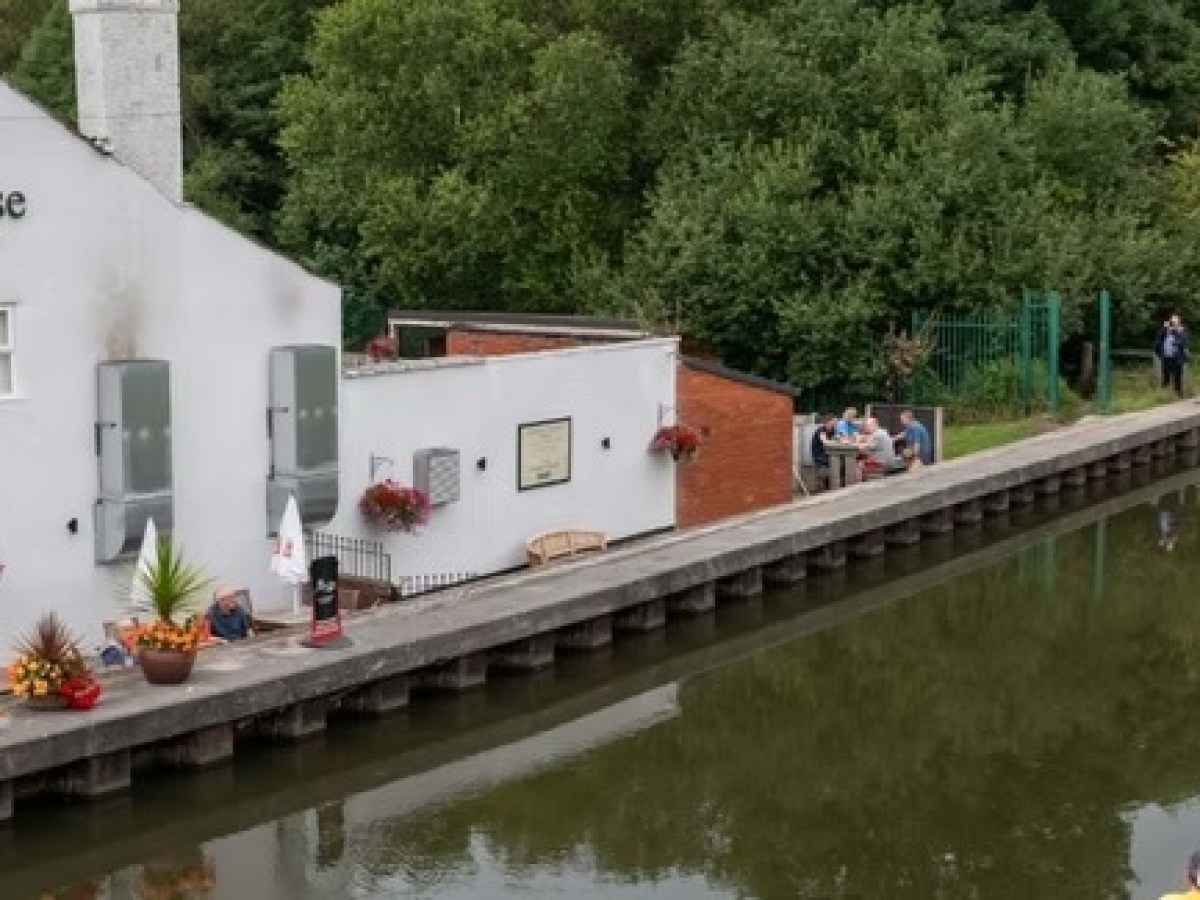 Canal with cyclists and a riverside pub, trees lining the water.