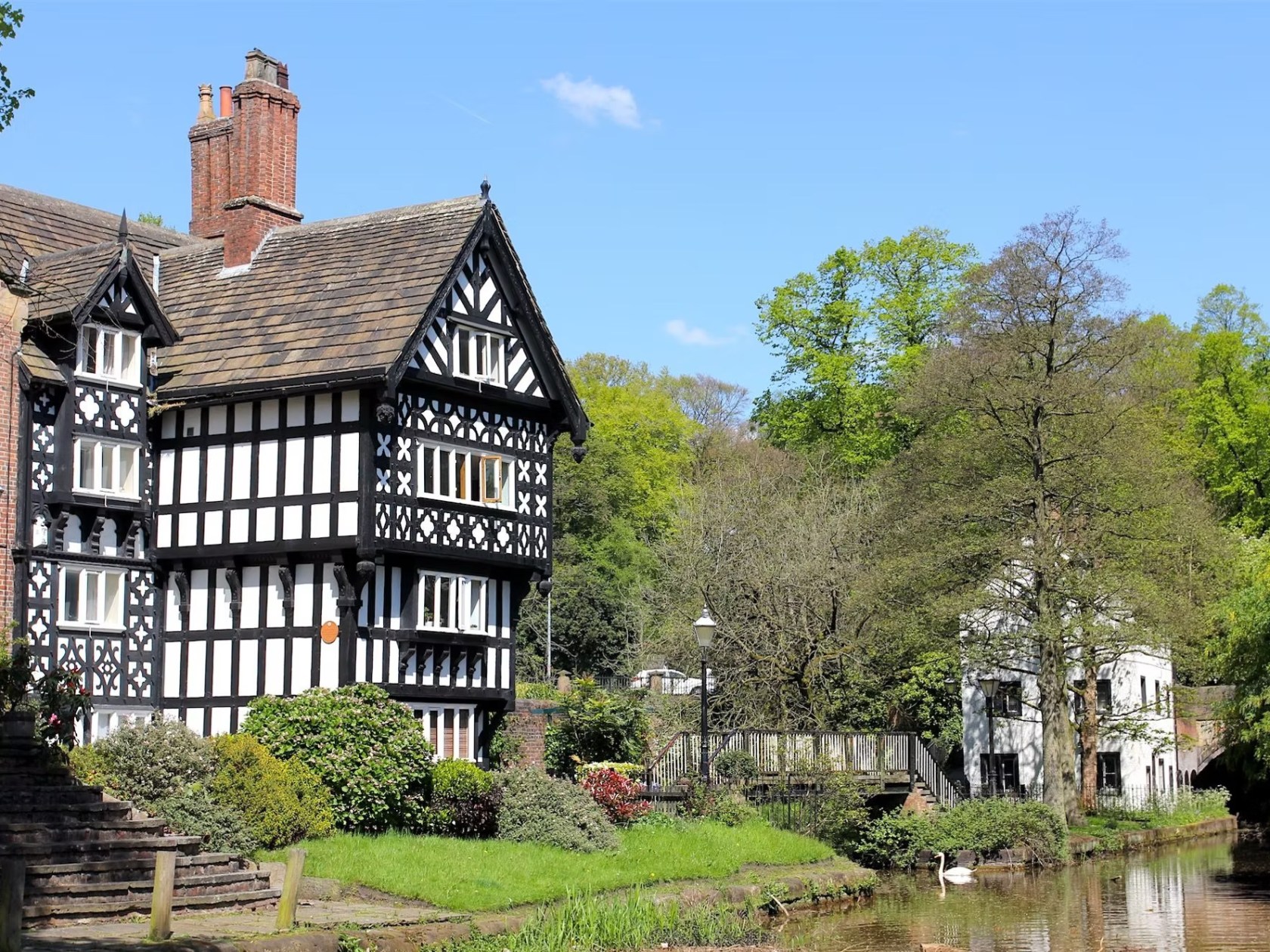 Tudor-style house by a canal, surrounded by trees, under a clear sky.