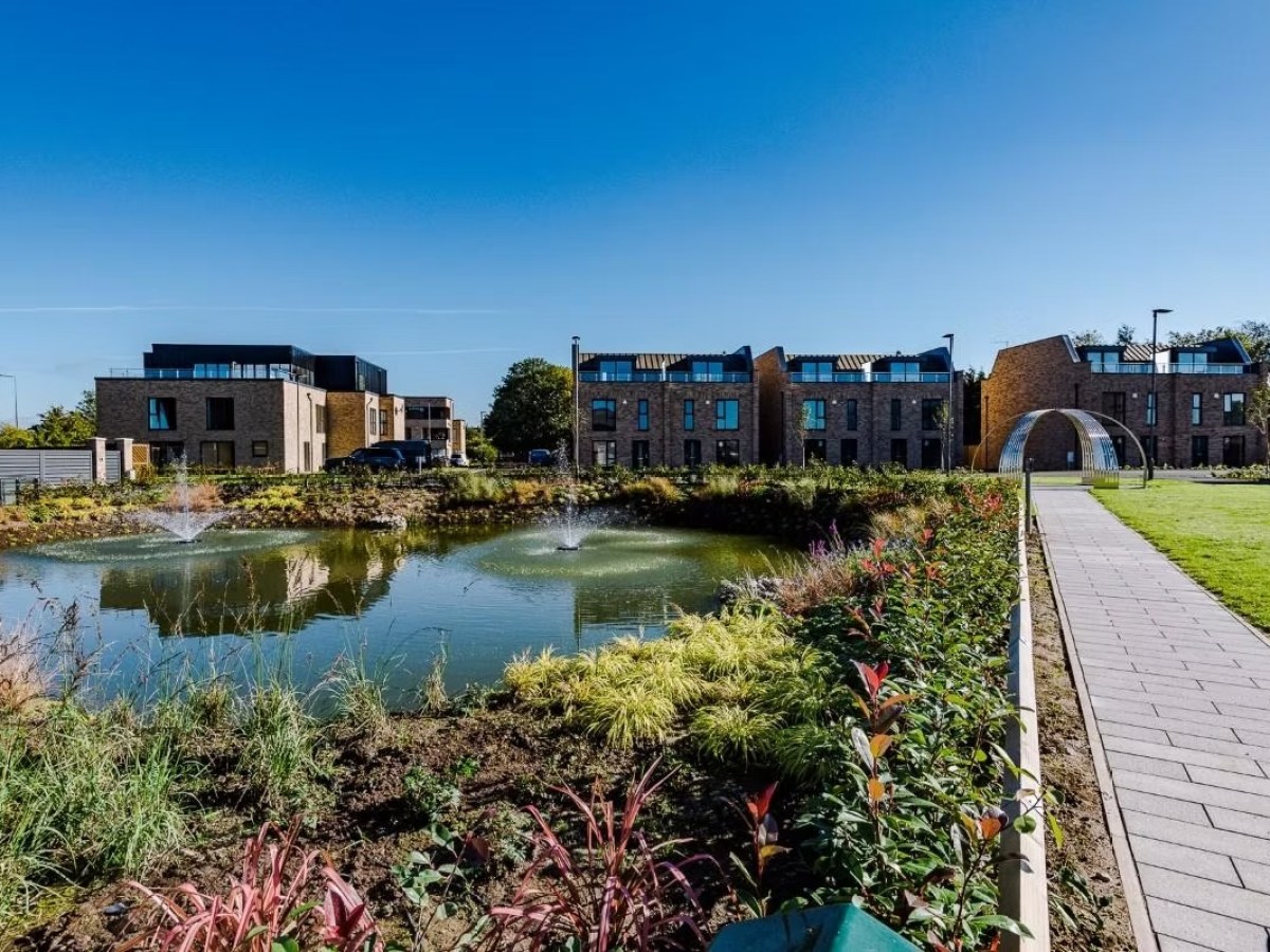 Modern buildings with a pond and landscaped garden under a clear blue sky.