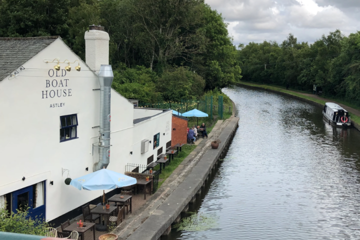 Canal with boat beside a building labeled 'Old Boat House' and outdoor seating, surrounded by trees.