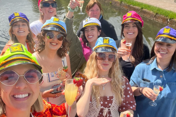 Group of people celebrating on a boat, wearing colorful captain hats and holding drinks.