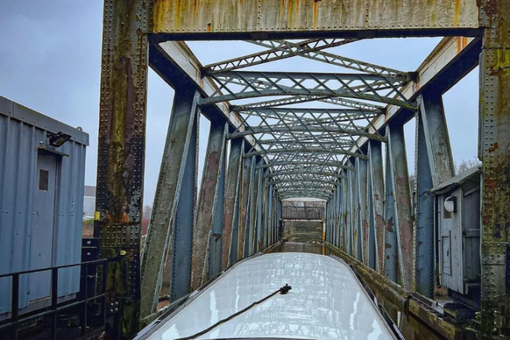 Boat passing under a rusty metal truss bridge.