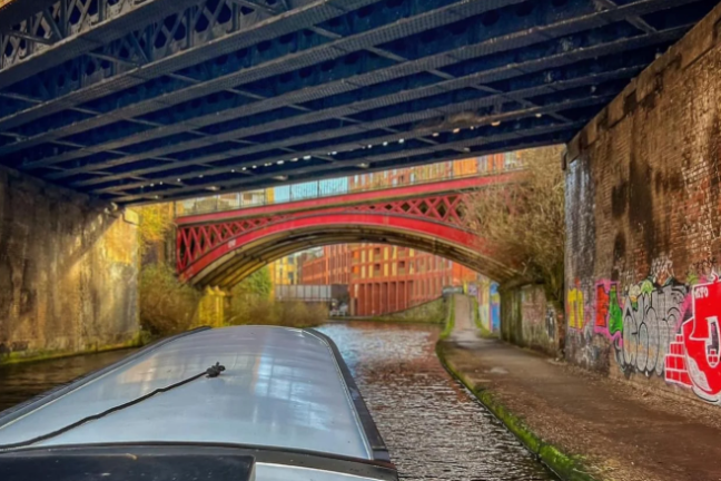 View from boat under bridges on a canal with colorful graffiti walls.